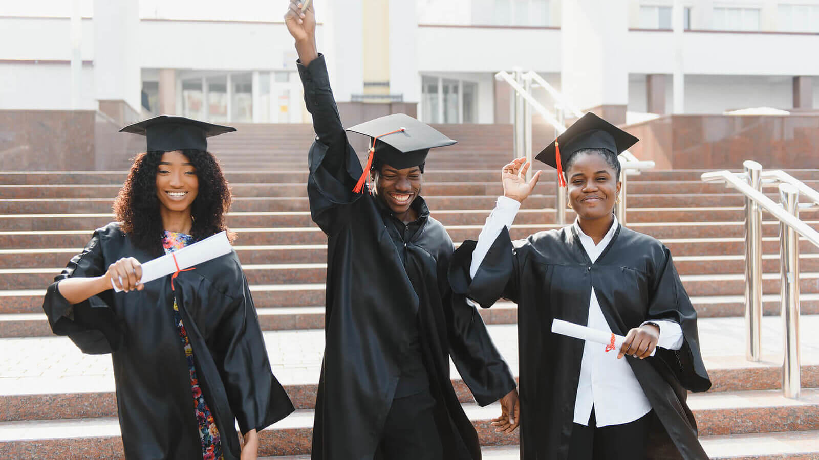 three students in cap and gown celebrating graduation